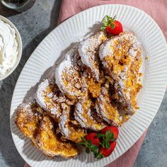 a plate with powdered sugar covered pastries and strawberries next to bowls of whipped cream