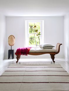 a bed sitting in the middle of a white room next to a vase with flowers