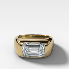 a yellow gold ring with an emerald cut diamond in the center and two smaller diamonds on each side