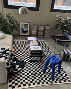 a living room with black and white checkered rugs on the floor, two couches, coffee table, bookshelf and chairs