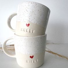 two white coffee mugs with red hearts and the words lucky written on them are stacked next to each other