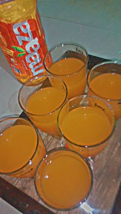 six glasses filled with orange juice on top of a wooden tray next to a bottle