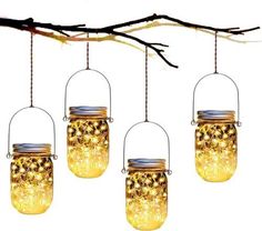 three mason jars hanging from a tree branch with lights inside them and some branches in the background