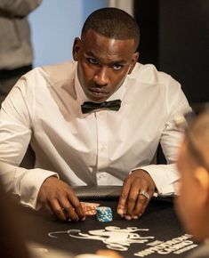 a man wearing a bow tie playing cards at a table with other people around him