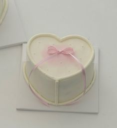 a heart shaped cake sitting on top of a white plate with a pink ribbon around it