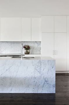 a kitchen with white cabinets and marble counter tops, along with a vase filled with flowers