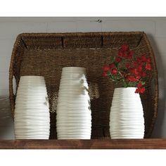 three white vases sitting on top of a wooden shelf next to a basket filled with red flowers