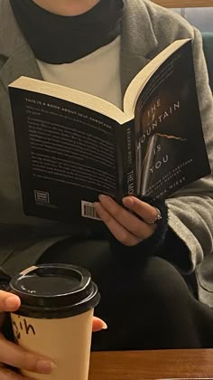 a woman reading a book while holding a coffee cup