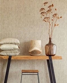 a wooden table topped with two vases filled with flowers next to pillows and blankets