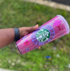 a person holding a pink starbucks drink in their left hand and green grass in the background