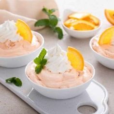 four small white bowls filled with food and garnished with orange slices on top