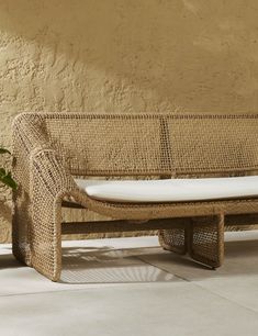 a wicker bench sitting next to a wall with a potted plant on it