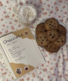 chocolate chip cookies are on a plate next to a recipe book and glass of milk