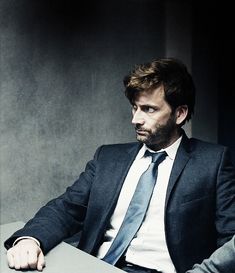 a man in a suit and tie sitting at a table with his hand on the desk