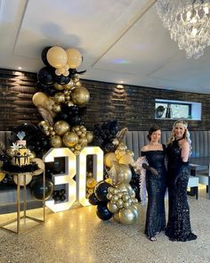 two women standing next to each other in front of balloons that spell out the number 30