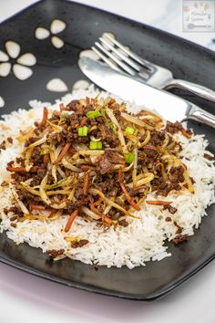 a black plate topped with white rice and ground beef next to a knife and fork