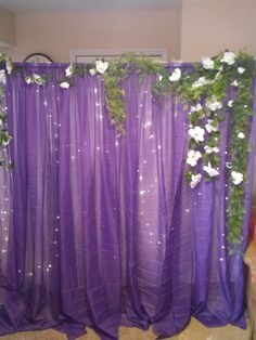 a purple curtain with white flowers and greenery on the top is in front of a window