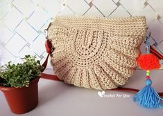 a crocheted purse sitting on top of a table next to a potted plant