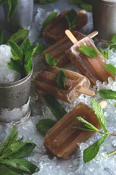 three popsicles with mint leaves on top of ice and silver cups filled with water