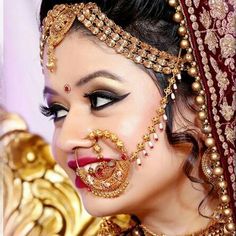 a woman wearing a gold and red bridal outfit with jewelry on her face, looking to the side