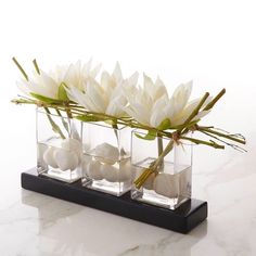 three clear vases with flowers in them on a marble countertop, one is filled with rocks and the other has grass