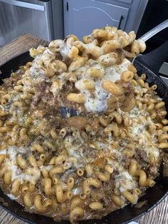 a skillet filled with macaroni and cheese on top of a wooden table