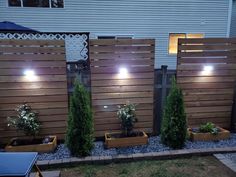 the lights are on in the garden by the house's privacy fence, which is lined with wooden planters