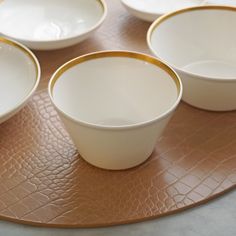 four white bowls are sitting on top of a brown place mat with gold rims