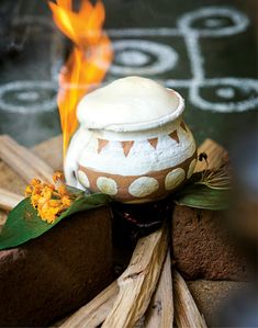 a white pot sitting on top of a pile of wood next to a burning fire