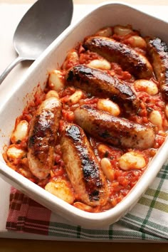 some sausages and beans are in a white casserole dish on a table