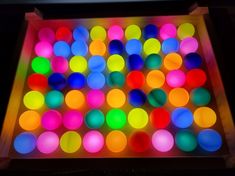 a box filled with lots of different colored balls on top of a wooden table next to a black wall