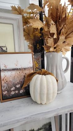 a white vase filled with lots of leaves next to a framed photo and a pumpkin