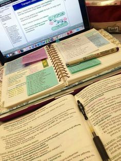 an open book sitting on top of a desk next to a laptop computer and pen