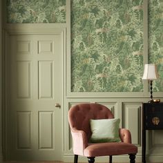 a pink chair sitting in front of a green wallpapered room with a lamp