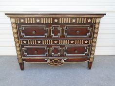 an antique chest of drawers with gold trimmings and stars on the top, sitting in front of a garage door