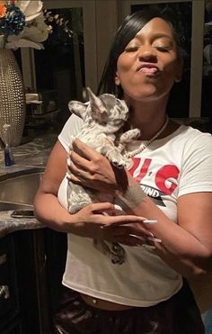 a woman is holding a small dog in her arms and making a funny face while standing next to a sink