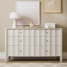 a white dresser with two lamps and pictures on the wall