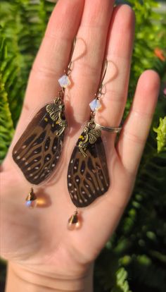 a hand holding two brown and white butterfly shaped earrings