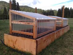 a wooden box with plants growing in it on top of some grass and fenced in area