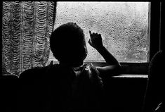 black and white photograph of child looking out window with raindrops on the windowsill