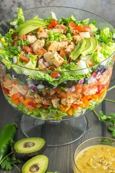 a salad with chicken, lettuce, carrots and avocado in a glass bowl