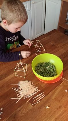 a young boy sitting at a kitchen table making geometric shapes out of sticks and vegetables