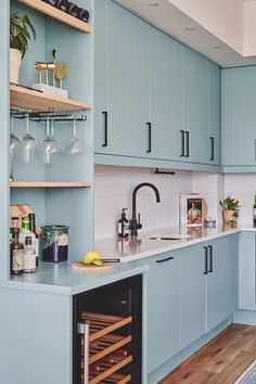 a kitchen with blue cabinets and wine glasses on the counter top, next to a sink