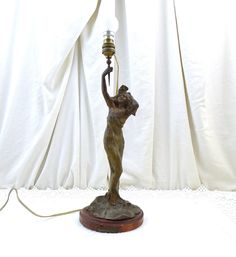 a bronze statue holding a lamp on top of a wooden base with a white curtain behind it