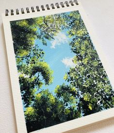 a spiral notebook with an image of trees and sky in the background on a white surface