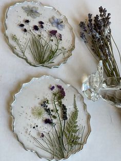 two plates with dried flowers on them next to a glass vase