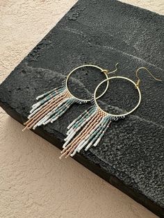 Unleash your inner bohemian spirit with these captivating beaded fringe earrings. Featuring a stunning gold hoop base that elegantly frames a cascade of mesmerizing teal and rose gold fringe, these earrings are sure to turn heads wherever you go. Each bead is meticulously selected and strung, creating a vibrant interplay of color and texture with every movement. More than just an accessory, these earrings are a testament to artisan skill. The meticulous craftsmanship ensures a flawless piece tha Bohemian Dangle Fringe Hoop Earrings, Bohemian Fringe Dangle Hoop Earrings, Bohemian Rose Gold Dangle Jewelry, Bohemian Rose Gold Dangle Earrings, Bohemian Style Rose Gold Jewelry For Festivals, Rose Gold Bohemian Jewelry For Festivals, Bohemian Style Jewelry, Gold Fringe, Boho Fashion Bohemian