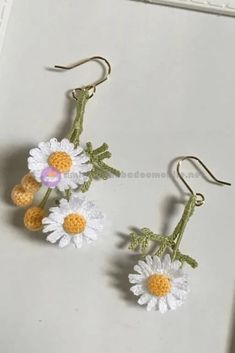 two crocheted daisies are hanging from hooks on a white surface, one is yellow and the other is white