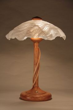 a wooden table lamp with a glass shade on it's base and a white fabric draped over the top