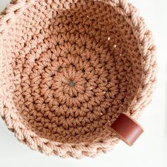 a crocheted basket with a brown leather handle on the bottom, sitting on a white surface